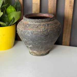 Peut inclure: Un pot en céramique rustique de couleur brun foncé avec une forme légèrement arrondie. Le pot a une surface rugueuse et texturée et semble très vieux.