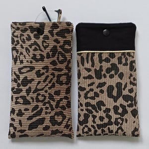 Peut inclure: Deux pochettes rectangulaires en velours côtelé à motif léopard beige et marron foncé. La pochette de gauche possède une fermeture à pression noire. Celle de droite présente une partie supérieure en tissu noir uni, un liseré doré et une pression.
