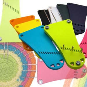 Puede incluir: Surtido de herramientas de telar de plástico de colores. Las herramientas tienen forma de lágrima con una serie de agujeros a lo largo del borde. Las herramientas están dispuestas en semicírculo con una alfombra tejida de arcoíris en el fondo.