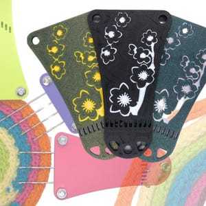 Peut inclure: Quatre métiers à tisser en plastique de couleurs différentes avec un motif floral. Les métiers à tisser sont disposés en cercle avec un cercle crocheté au centre.