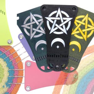 Op de afbeelding: Een verzameling kleurrijke weefgereedschappen en accessoires. De afbeelding toont verschillende weefgereedschappen in groen, roze en paars. De gereedschappen hebben een pentagram- en halve maan-ontwerp. Er is ook een regenboogkleurig geweven stuk te zien.