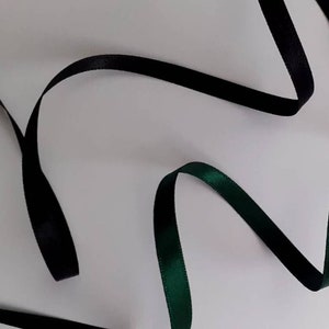 May include: Two satin ribbons, one black and one dark green, are arranged in a wavy pattern on a white background.