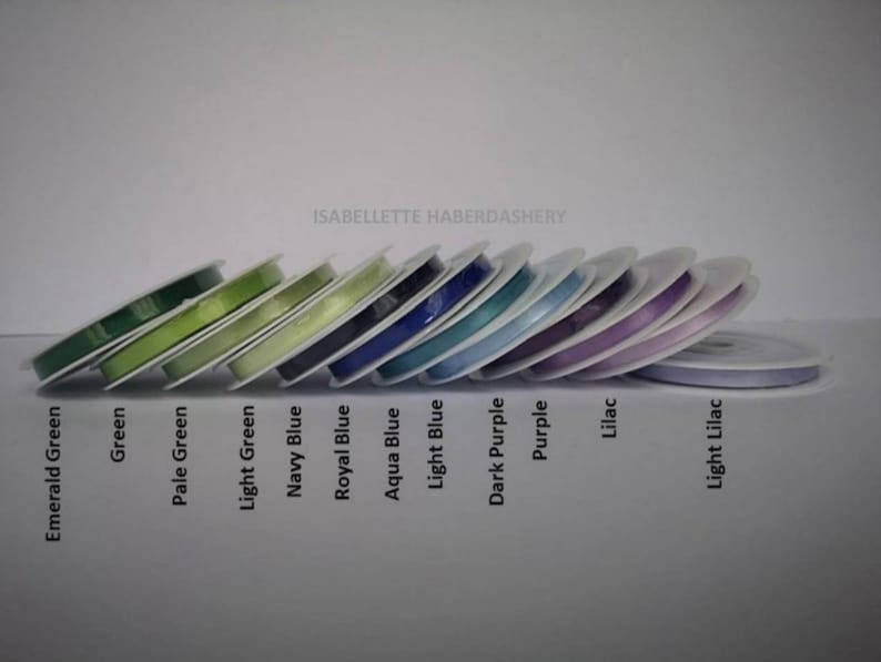 May include: A collection of spools of ribbon in various colors, including emerald green, green, pale green, light green, navy blue, royal blue, aqua blue, light blue, dark purple, purple, lilac, and light lilac. The spools are arranged in a row, with the darkest colors on the left and the lightest colors on the right. The text "ISABELLETTE HABERDASHERY" is visible at the top of the image.