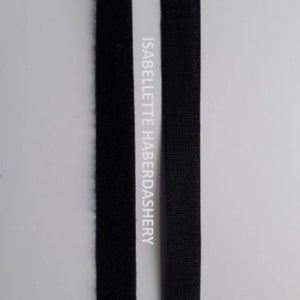 May include: Two black strips of hook and loop tape, also known as Velcro, are shown side-by-side. The tape on the left is the fuzzy side, while the tape on the right is the hook side. The text "ISABELLETTE HABERDASHERY" is printed on the white background behind the tape.