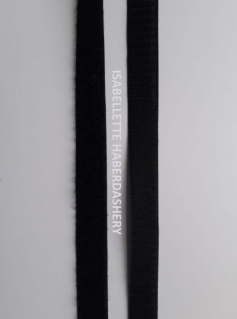 May include: Two black strips of hook and loop tape, also known as Velcro, are shown side-by-side. The tape on the left is the fuzzy side, while the tape on the right is the hook side. The text "ISABELLETTE HABERDASHERY" is printed on the white background behind the tape.