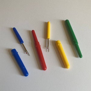 May include: Five thread snips in different colors: blue, red, yellow, and green. The snips are closed and have a small red dot on the tip of the blade.