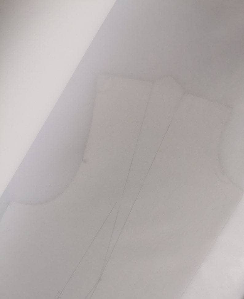May include: A light-colored sewing pattern, possibly for a bodice or top, is visible. The pattern is drawn on a translucent material, with visible lines and shapes indicating the design. The overall image is softly lit, with a focus on the pattern's details.
