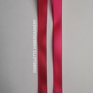 May include: Two satin ribbons, one in a deep pink and the other in a slightly lighter shade of pink. The ribbons are both about 1 cm wide and are lying flat on a white surface. The text "ISABELLETTE HABERDASHERY" is printed vertically on the left side of the image.