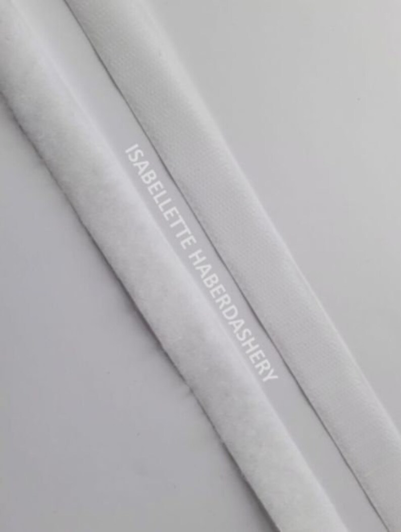 May include: Two white fabric trims, one with a fuzzy texture and the other smooth, with the text "ISABELLETTE HABERDASHERY" printed on the smooth trim.