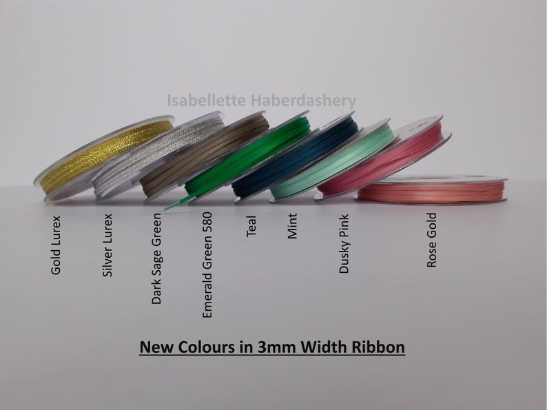 May include: A selection of 3mm wide ribbon spools in various colors, including gold, silver, teal, mint, dusky pink, and rose gold. The text "New Colors in 3mm Width Ribbon" and "Isabellette Haberdashery" are visible on the image.