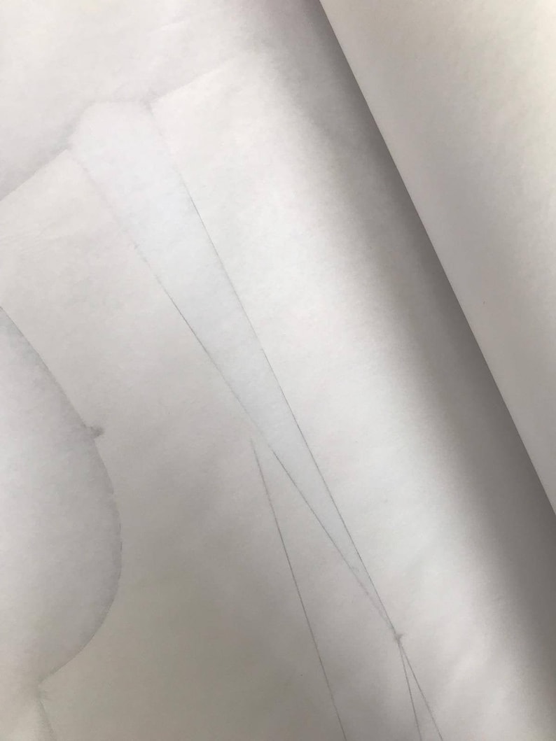 May include: Close-up of a white paper pattern with faint pencil markings. The pattern is partially rolled, revealing the texture and layers of the paper. The image suggests a sewing or crafting project.