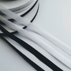 May include: Close-up of three rolls of black and white fabric trim. The trim is arranged in a stack, with the black trim on top and the white trim on the bottom. The trim is likely used for sewing or crafting projects.