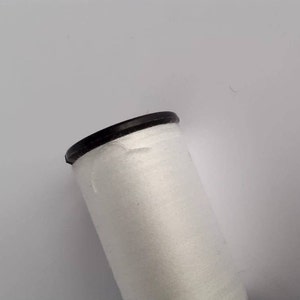 Op de afbeelding: Een witte spoel garen met een zwarte plastic bovenkant.