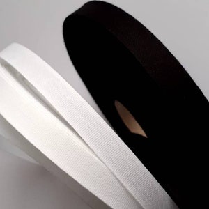 Könnte beinhalten: Drei Rollen weißes und schwarzes Gummiband. Das weiße Band ist in der Mitte gefaltet und das schwarze Band ist aufgerollt.