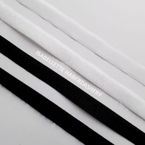 May include: Two strips of black hook and loop tape and one strip of white hook and loop tape. The tape is laid out on a white surface. The text "ISABELLETTE HABERDASHERY" is printed on the surface.
