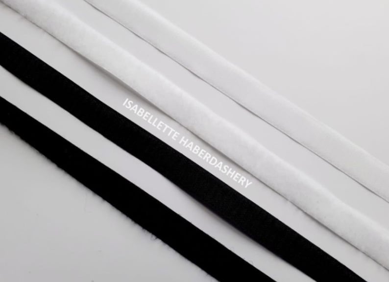 May include: Two strips of black hook and loop tape and one strip of white hook and loop tape. The tape is laid out on a white surface. The text "ISABELLETTE HABERDASHERY" is printed on the surface.
