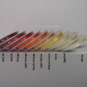 May include: A collection of spools of ribbon in various colors, including burgundy, red, orange, yellow, cream, ivory, eggshell, and white. The spools are arranged in a row from darkest to lightest.