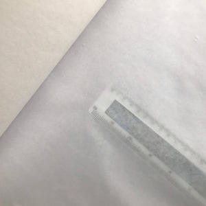 May include: A close-up shot of white fabric with a ruler placed diagonally across the material. The ruler is gray with black markings, indicating measurements in inches and centimeters. The fabric appears soft and slightly textured.
