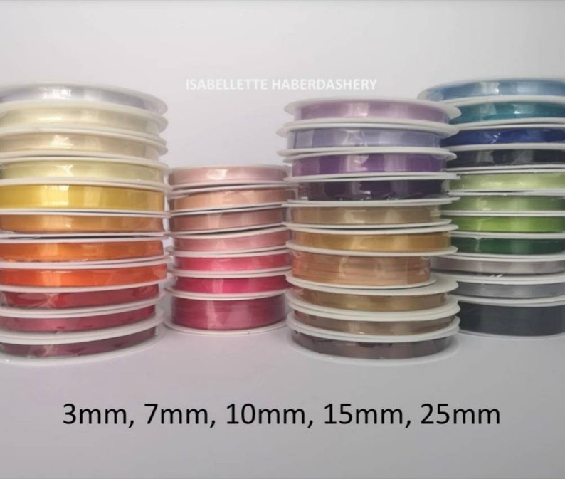May include: Spools of satin ribbon in various colors and widths, including 3mm, 7mm, 10mm, 15mm, and 25mm.  The ribbon is arranged in stacks of different colors, including white, yellow, orange, red, pink, purple, blue, green, and black.