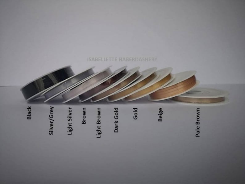 May include: Spools of ribbon in various colors, including black, silver, light silver, brown, light brown, dark gold, gold, beige, and pale brown. The spools are labeled with the corresponding colors. The text "ISABELLETTE HABERDASHERY" is visible at the top of the image.