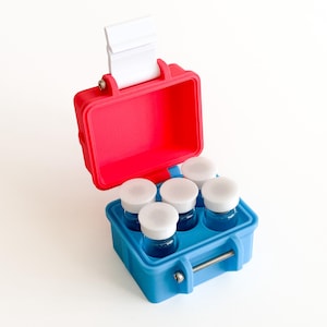 May include: A red and blue plastic carrying case with a white handle, open to reveal five small glass bottles with white lids. The case is designed to hold the bottles securely, suggesting a travel or storage container for small items.