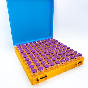 May include: A yellow storage case with a bright blue lid containing a grid of eighty-one small, clear glass vials. Each vial is topped with a purple cap and arranged in a nine-by-nine square formation within the rectangular container.