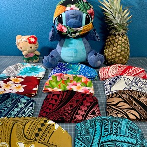 May include: A collection of 10 colorful fabric headbands with various patterns, including floral, geometric, and tribal designs. The headbands are arranged on a gray surface, with a blue plush toy and a pineapple in the background.