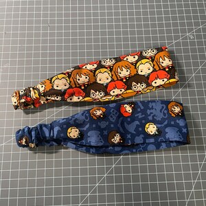 May include: Two fabric headbands with a Harry Potter theme. One headband is orange and brown with a pattern of Harry Potter characters. The other headband is blue with a pattern of Harry Potter characters and symbols.