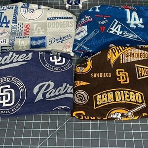 May include: A set of eight baseball-themed fabric headbands. The headbands feature various team logos, including the Los Angeles Dodgers, San Diego Padres, and Detroit Tigers. The headbands are made of a soft, comfortable fabric and are perfect for showing your team spirit.