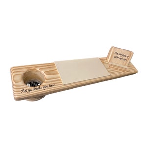 Op de afbeelding: Een houten dienblad met een ingebouwde bekerhouder en een klein plankje voor een telefoon of tablet. Het dienblad heeft de tekst "Put ya drink right here" en "Put dat phone or tablet right here" gegraveerd.