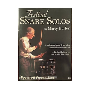 May include: A black and white book cover with the title "Festival Snare Solos" by Marty Hurley. The cover features a photo of a man playing a snare drum. The book is a revised edition and includes 9 rudimental snare drum solos for intermediate to advanced players.