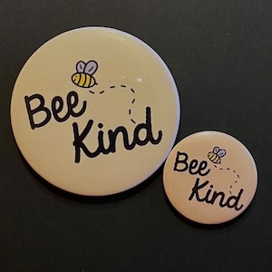 May include: Two beige round buttons with a black bee and the text "Bee Kind" in black lettering.