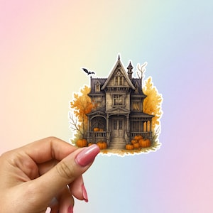 May include: A sticker featuring a detailed illustration of a spooky house with a bat flying overhead. The house is surrounded by pumpkins and autumn foliage, creating a Halloween or fall theme. The color palette includes shades of brown, orange, and black.