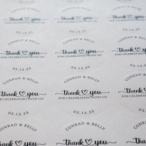 Peut inclure: Gros plan sur des autocollants ronds blancs avec du texte noir. Les autocollants indiquent "Thank you" avec un c&oelig;ur, "For celebrating with us!" et la date "03.13.25". Les noms "Conrad & Belly" sont &eacute;galement imprim&eacute;s.
