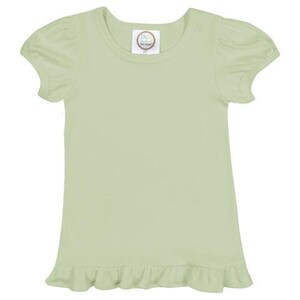 May include: A light green short-sleeved t-shirt with a ruffled hem. The shirt has a round neckline and a small, round label with the text "Baby Bella Boutique" on the front.