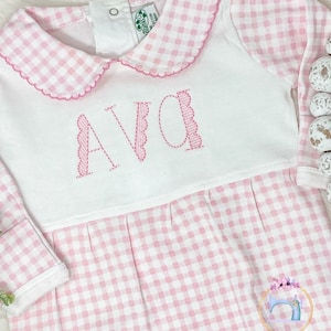 May include: Pink and white gingham baby onesie with a white collar and the name "AVA" embroidered in pink on the front.