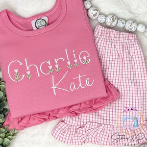 May include: Pink and white gingham ruffle shorts with a pink ruffle top that says "Charlie Kate" with embroidered tulips.