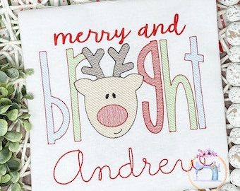 May include: A white embroidered Christmas shirt with the text "merry and bright" in red, green, and blue. A cartoon reindeer is in the middle of the text. The name "Andrew" is embroidered in red at the bottom.
