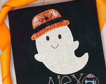 May include: Black t-shirt with a white ghost wearing an orange and black spiderweb hat. The name "Alex" is stitched in white below the ghost.