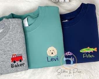May include: Three children's sweatshirts in gray, teal, and navy blue. The gray sweatshirt has a red fire truck and the name "Baker". The teal sweatshirt has a dog and the name "Levi". The navy blue sweatshirt has a fish and the name "Peter".