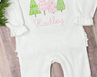 May include: White long-sleeved baby onesie with a ruffled hem and cuffs. The onesie features an embroidered design of four Christmas trees in pink and green with the name "Hadley" embroidered below.