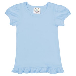 May include: A light blue baby t-shirt with short sleeves and a ruffled hem. The shirt has a small tag with the text "BB Boutique" on the front.