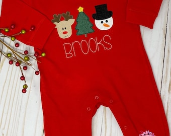 May include: Red long-sleeve baby onesie with a reindeer, Christmas tree, and snowman applique. The onesie has the name "Brooks" embroidered on the front.