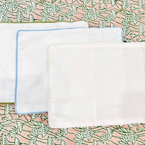 May include: Three white pillowcases with different colored trim. The pillowcases are arranged in a stack, with the largest at the bottom and the smallest at the top. The trim colors are green, blue, and white.