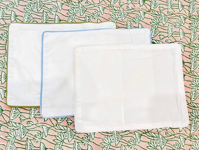 May include: Three white pillowcases with different colored trim. The pillowcases are arranged in a stack, with the largest at the bottom and the smallest at the top. The trim colors are green, blue, and white.