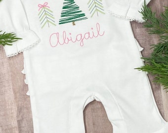 May include: White baby onesie with a green embroidered Christmas tree and pink bows. The onesie has a ruffled bottom and the name "Abigail" is embroidered below the tree.