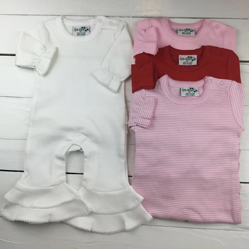 May include: Four baby onesies, one white with ruffled trim, one pink with white stripes, one red, and one pink with a bow. All onesies have a small tag with the text "Little Buns" on them.