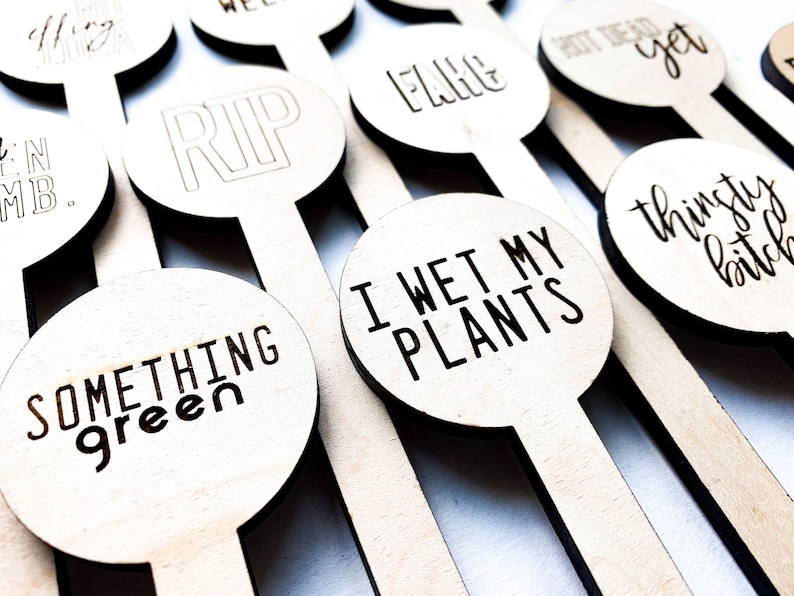 May include: A set of wooden plant markers with humorous and irreverent phrases, including "RIP", "I Wet My Plants", "Something Green", "Thinsty B*tch", and "Shot Dead Yet".