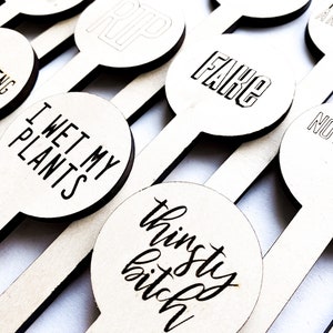 May include: A set of wooden plant markers with humorous phrases, including "I Wet My Plants", "Thinsty Bitch", "Something Green", "Fake", "RIP", "Tried and Died", and "Not Dead Yet".