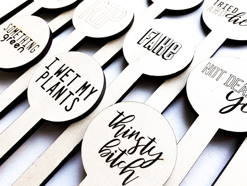 May include: A set of wooden plant markers with humorous phrases, including "I Wet My Plants", "Thinsty Bitch", "Something Green", "Fake", "RIP", "Tried and Died", and "Not Dead Yet".